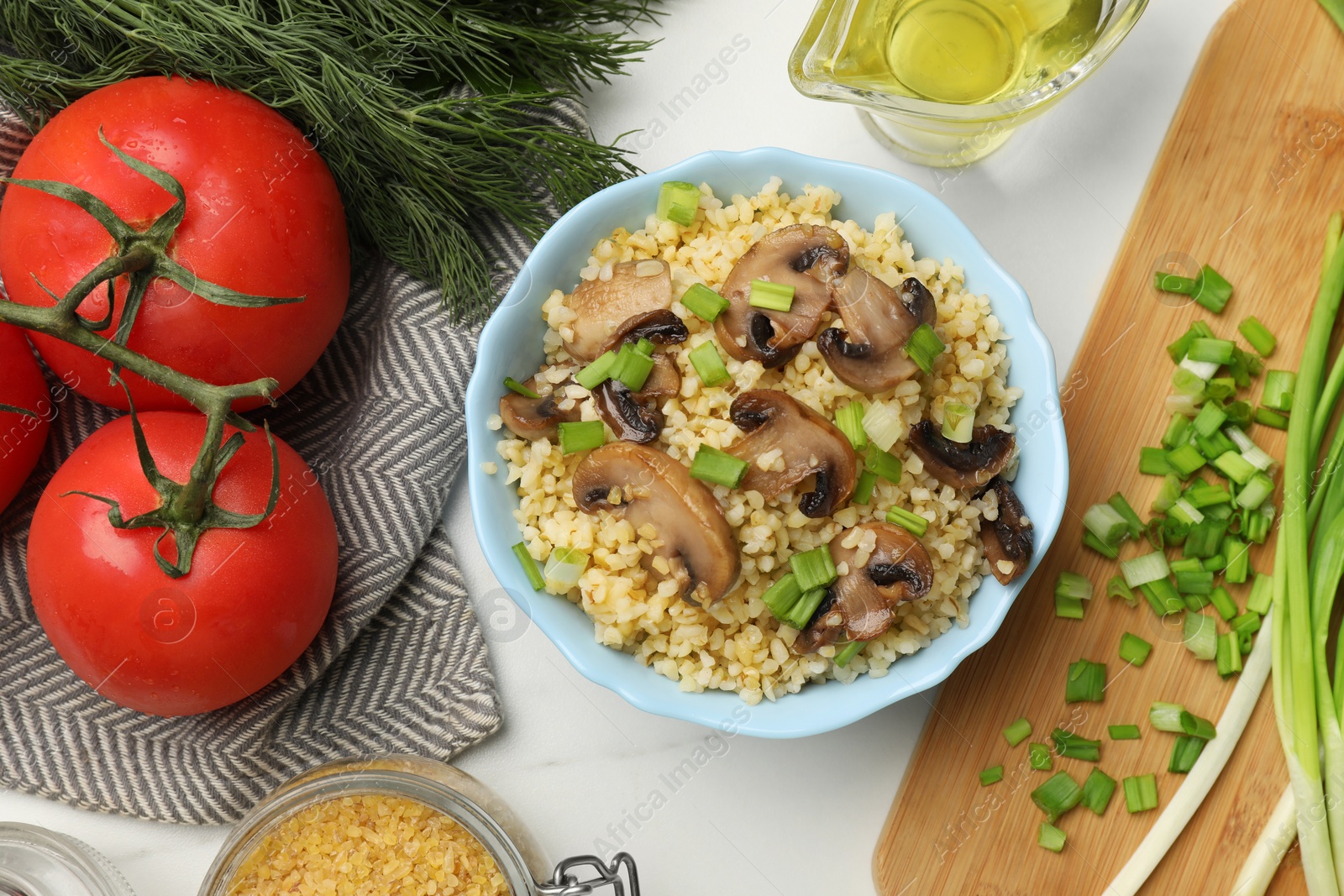 Photo of Delicious bulgur with mushrooms, green onion and other products on white table, flat lay