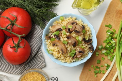 Photo of Delicious bulgur with mushrooms, green onion and other products on white table, flat lay