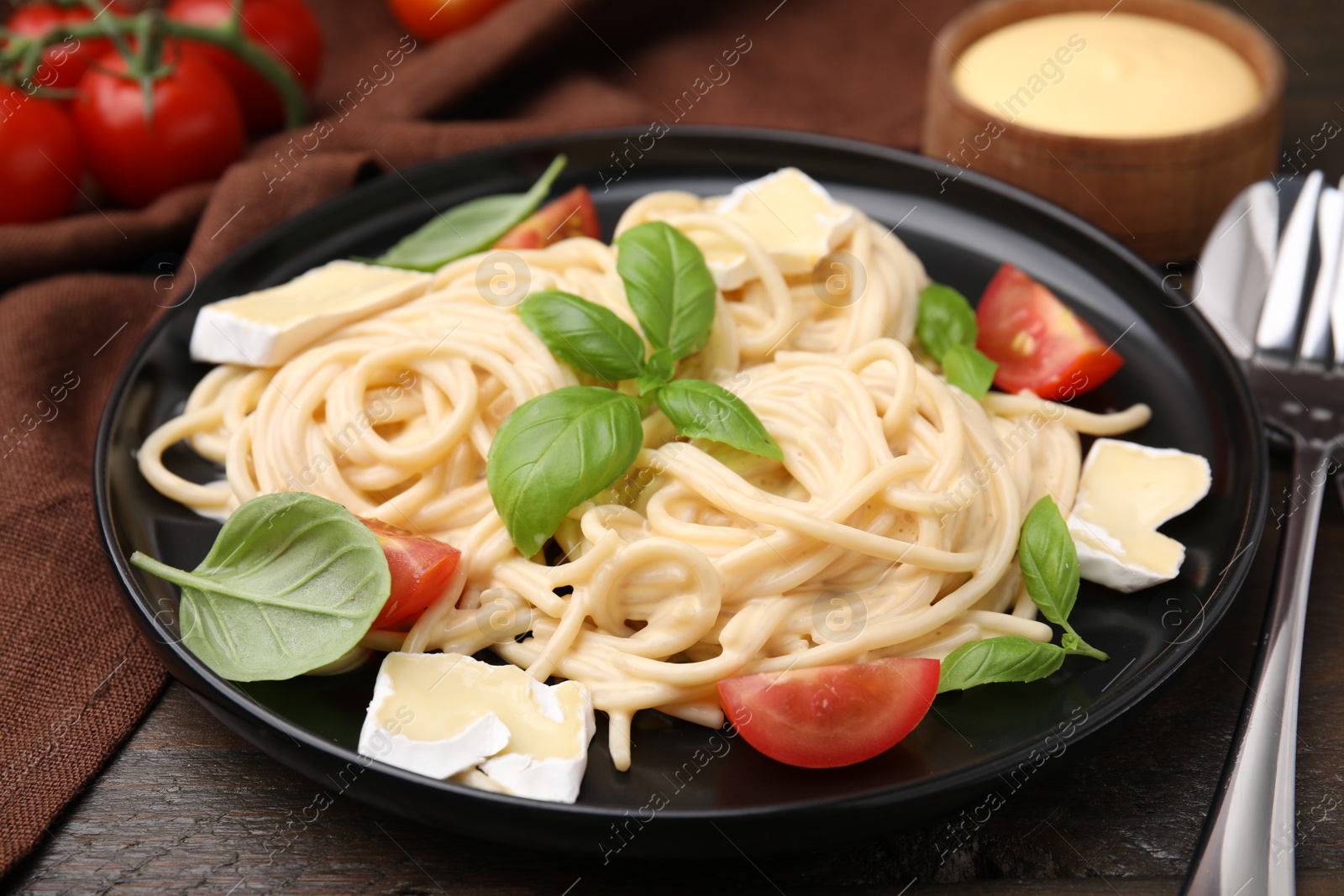 Photo of Delicious pasta with brie cheese, tomatoes and basil leaves served on table, closeup