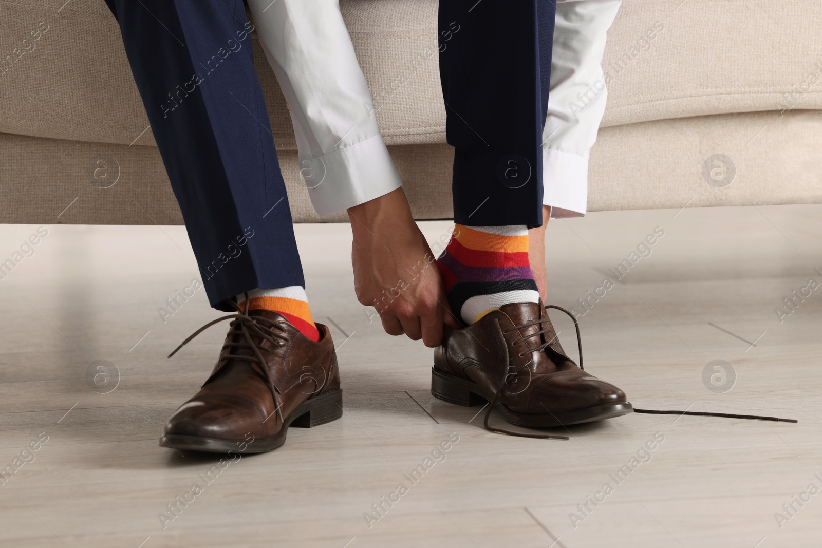 Photo of Man with colorful socks putting on stylish shoes indoors, closeup