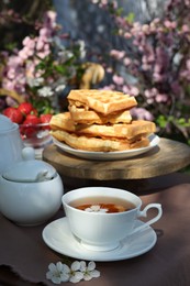 Photo of Beautiful spring flowers and freshly baked waffles on table served for tea drinking in garden