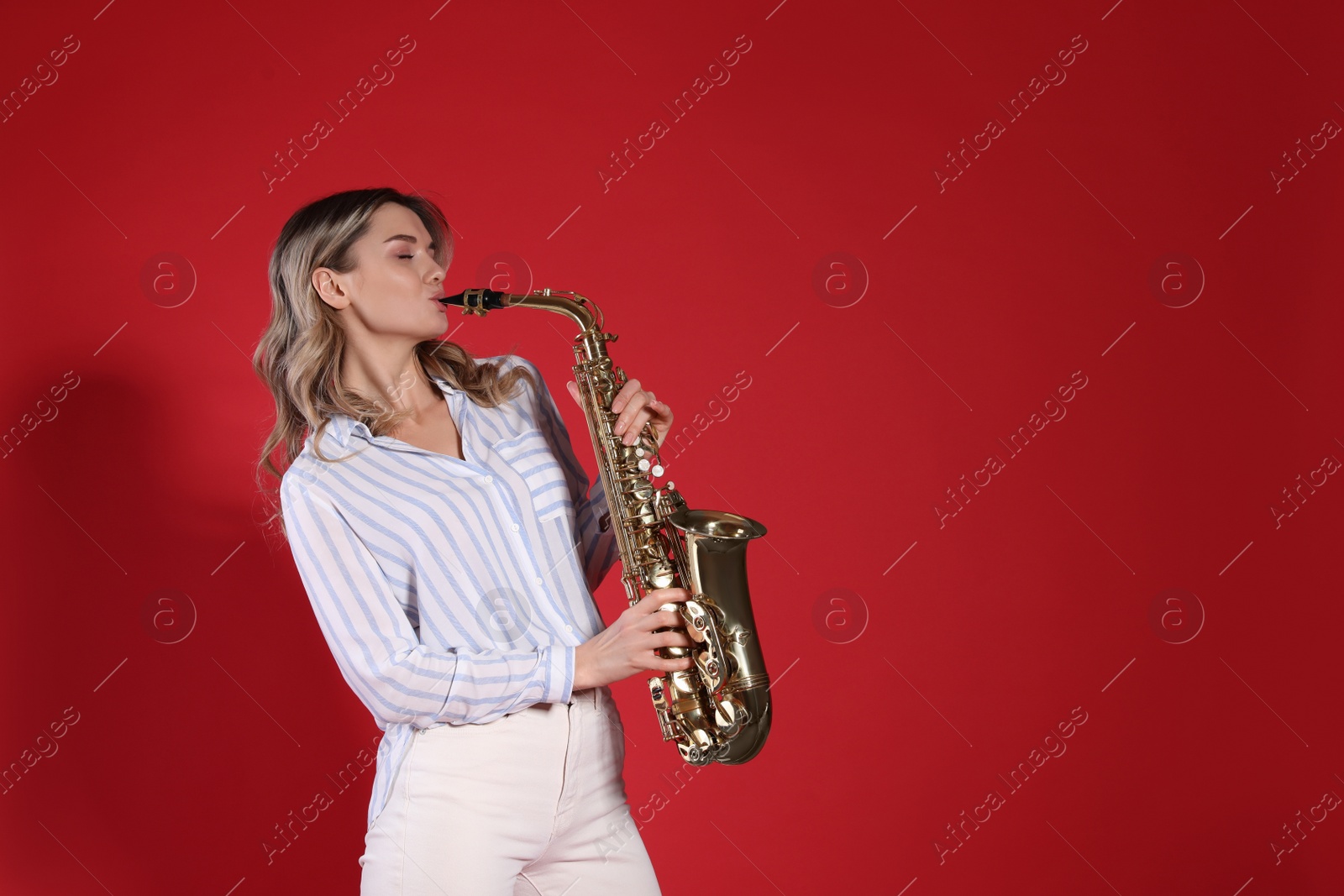 Photo of Beautiful young woman playing saxophone on red background. Space for text