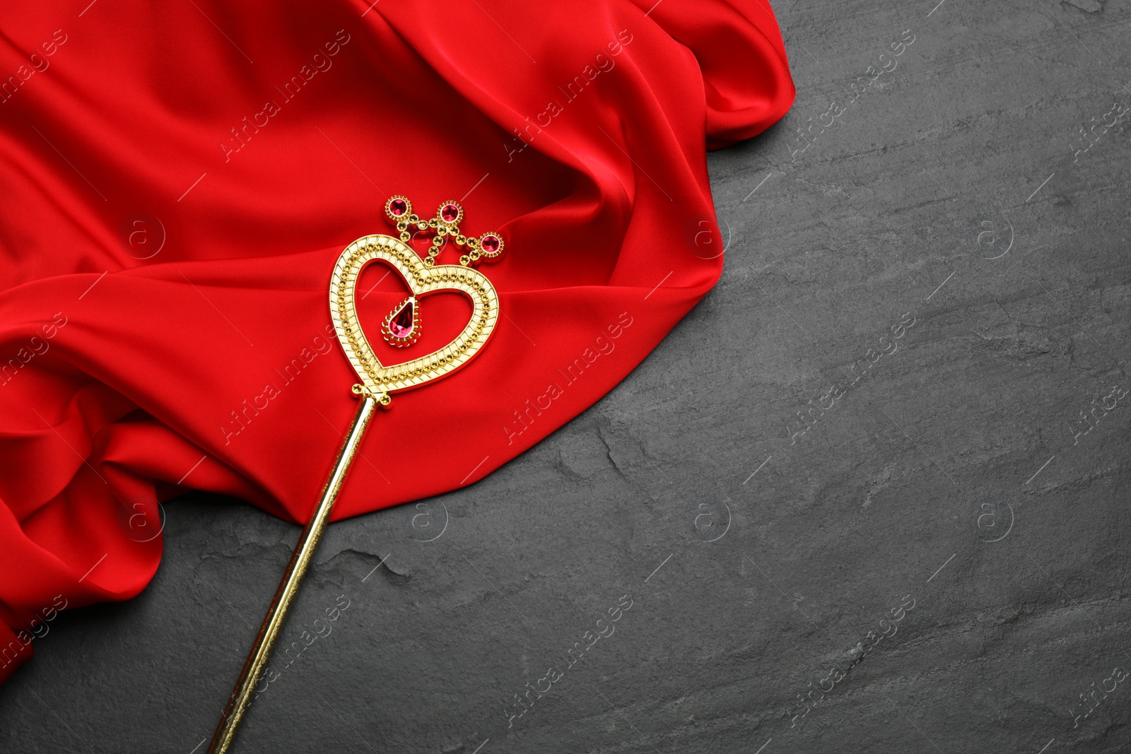 Photo of Beautiful golden magic wand and red fabric on black table, top view. Space for text