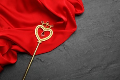 Beautiful golden magic wand and red fabric on black table, top view. Space for text