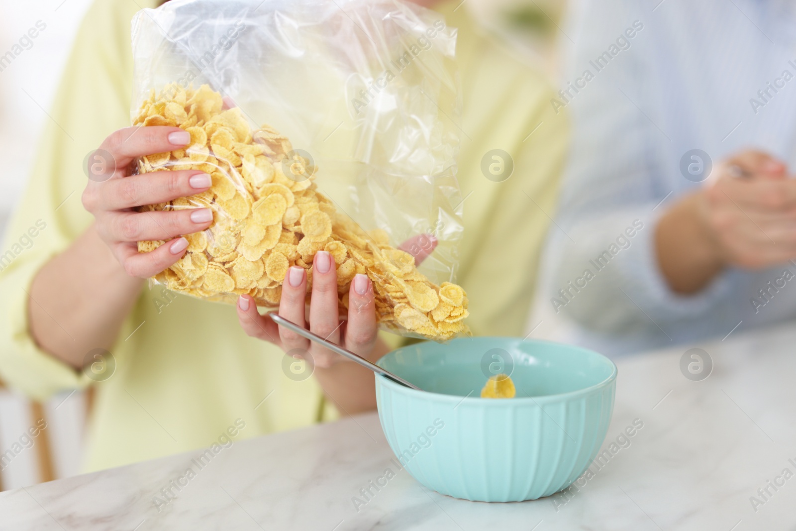 Photo of Making breakfast. Woman adding cornflakes into bowl at white marble table, closeup