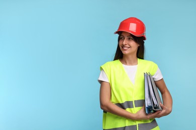 Architect in hard hat with folders on light blue background, space for text