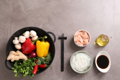 Wok, chopsticks and different products on grey textured table, flat lay. Space for text