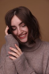 Portrait of beautiful young woman in warm sweater on brown background