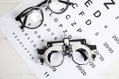 Photo of Trial frame, eye chart test and glasses on white wooden table, top view. Ophthalmologist tools