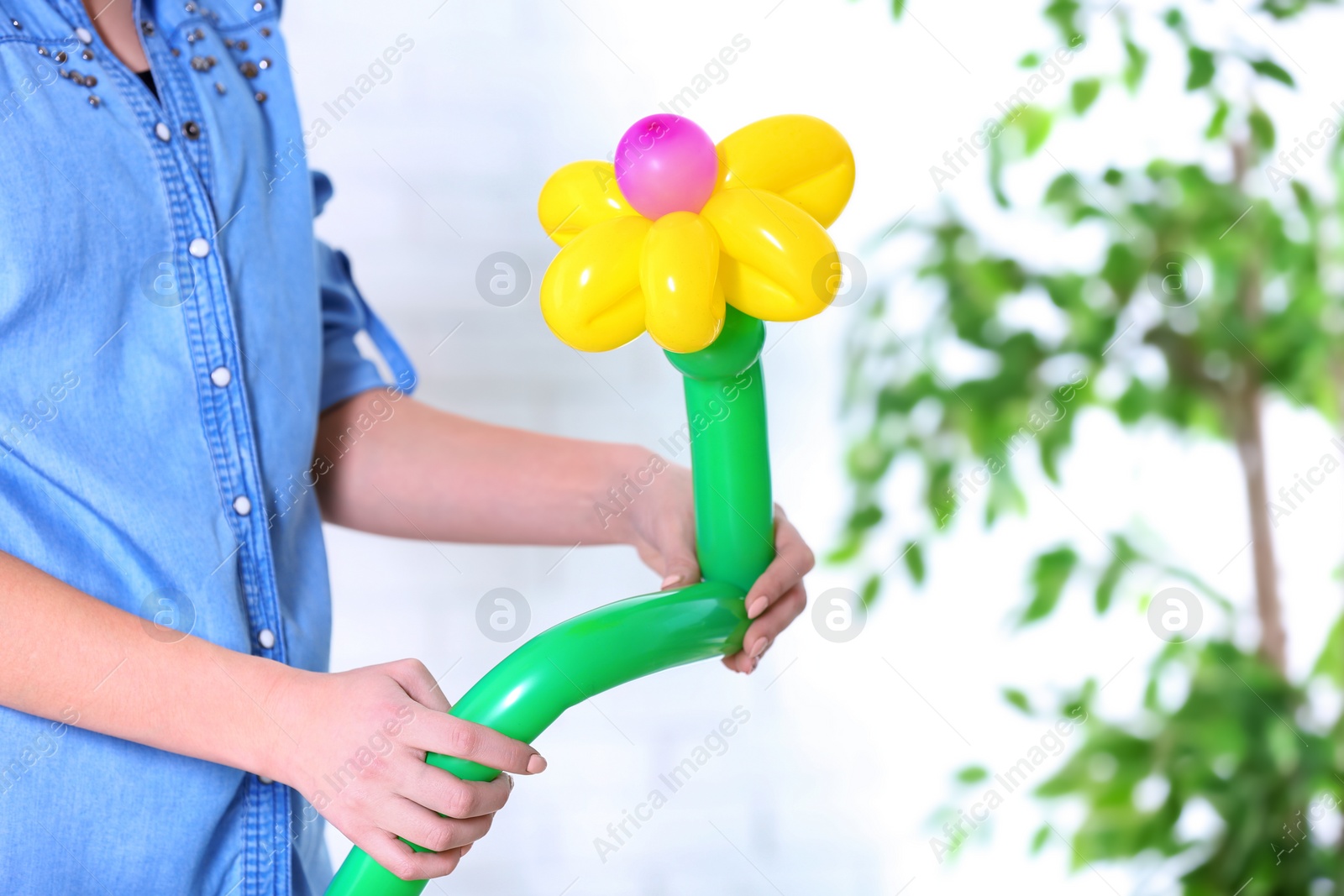 Photo of Woman making balloon figure on blurred background, closeup. Space for text