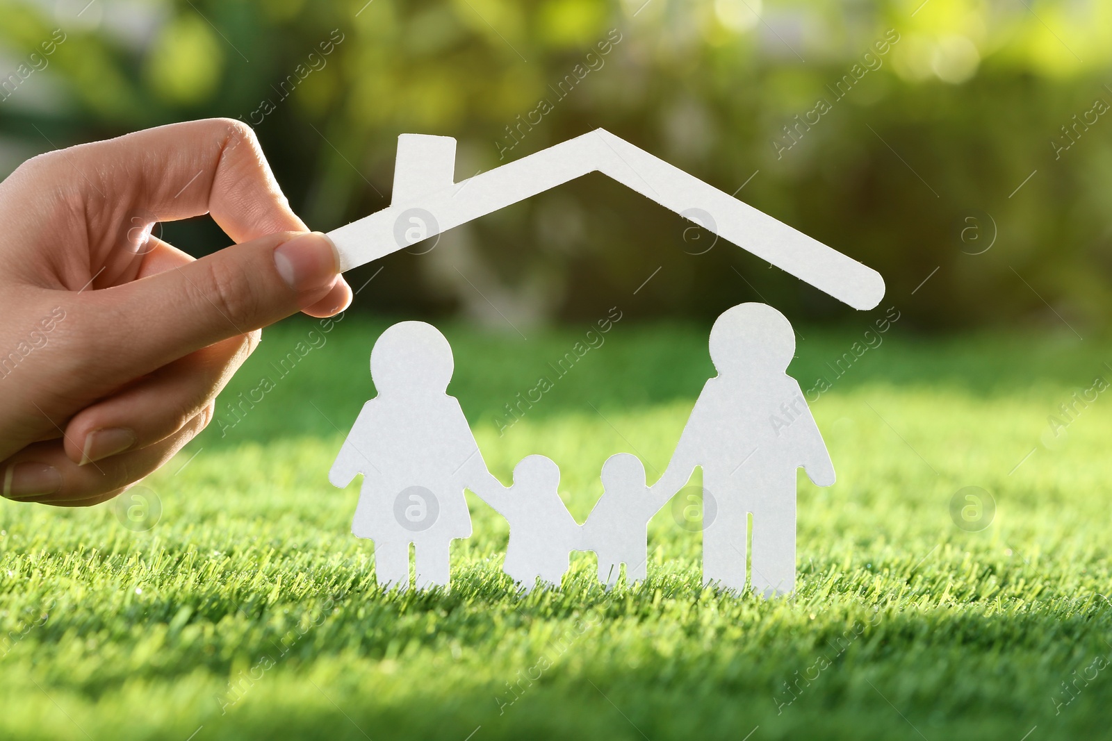 Photo of Woman holding paper roof over cutout of family on fresh grass, closeup. Life insurance concept