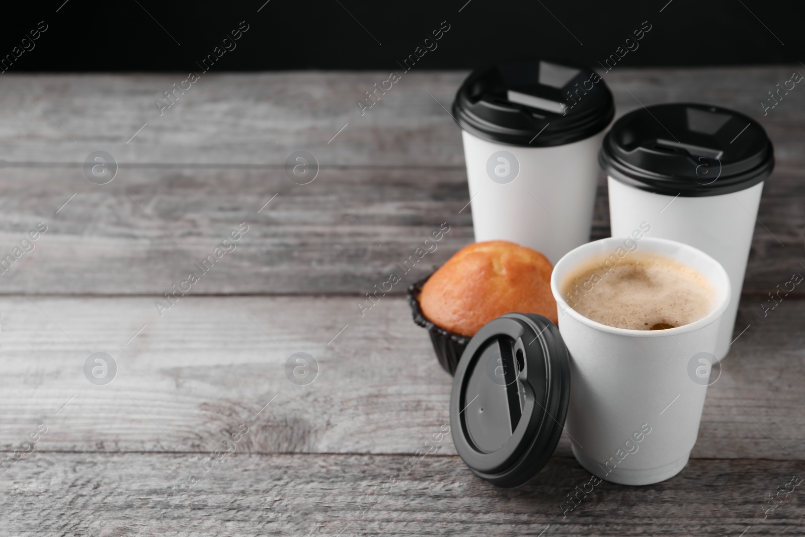 Photo of Coffee to go. Paper cups with tasty drink and muffin on wooden table, space for text