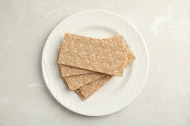 Photo of Plate with fresh rye crispbreads on light grey marble table, top view