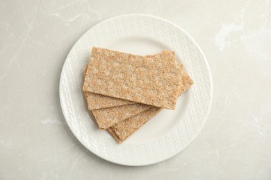 Plate with fresh rye crispbreads on light grey marble table, top view