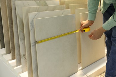 Photo of Man using tape measure while choosing tile in store, closeup