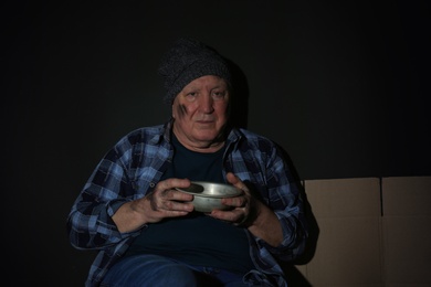 Photo of Poor senior man with bowl on dark background