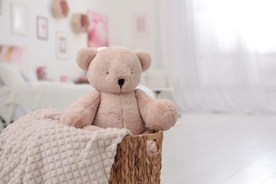 Photo of Cute teddy bear and blanket in wicker basket indoors