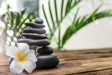Photo of Table with stack of stones, flower and blurred green leaves on background, space for text. Zen concept