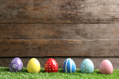 Photo of Painted Easter eggs on green grass against wooden background, space for text
