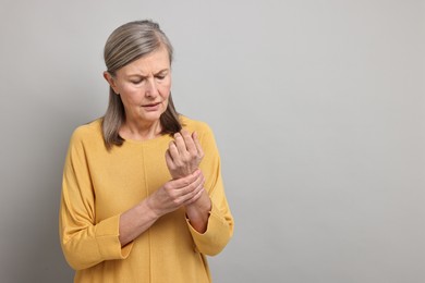 Photo of Arthritis symptoms. Woman suffering from pain in wrist on gray background, space for text