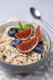 Photo of Oatmeal served with blueberries, mint and fig pieces on light grey table, closeup