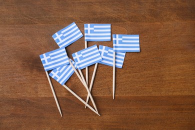 Photo of Small paper flags of Greece on wooden table, flat lay