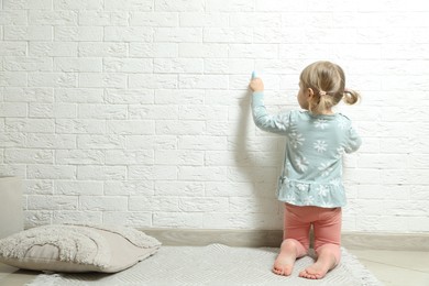 Photo of Little girl drawing on white brick wall indoors, back view and space for text. Child`s art