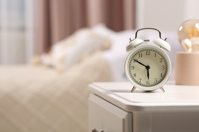 Photo of Stylish alarm clock on white nightstand indoors. Space for text