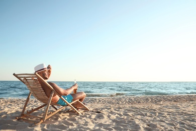 Photo of Young man relaxing in deck chair on beach near sea