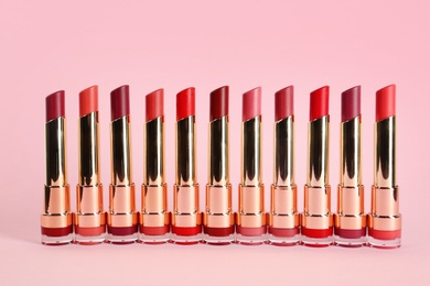Photo of Set of bright lipsticks in gold tubes on pink background