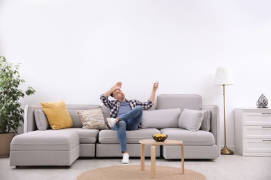 Photo of Young man with remote control suffering from heat under broken air conditioner at home