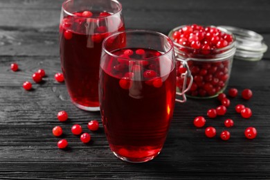 Photo of Tasty cranberry juice in glasses and fresh berries on black wooden table, closeup