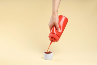 Photo of Woman squeezing tasty ketchup from bottle into bowl on beige background, closeup