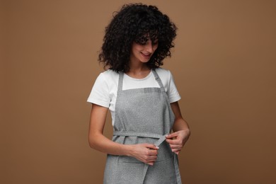 Photo of Happy woman wearing kitchen apron on brown background. Mockup for design