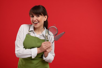 Photo of Happy confectioner in apron holding professional tools on red background. Space for text