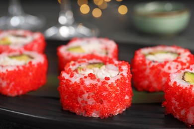 Photo of Delicious sushi rolls with tobiko on black plate, closeup