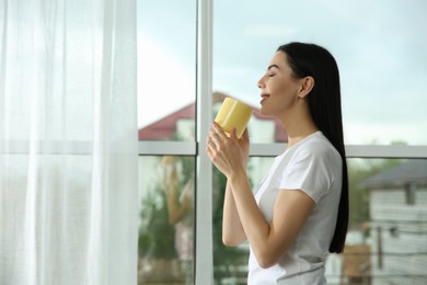 Photo of Young woman with cup of drink relaxing near window home, space for text