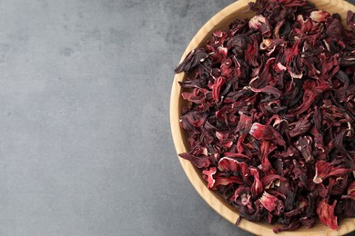 Photo of Hibiscus tea. Wooden bowl with dried roselle calyces on grey table, top view. Space for text