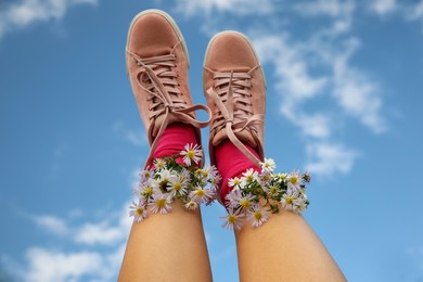 Photo of Woman with beautiful tender flowers in socks against blue sky, closeup