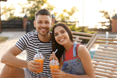Image of Happy couple with cups of refreshing drink resting in deck chairs outdoors