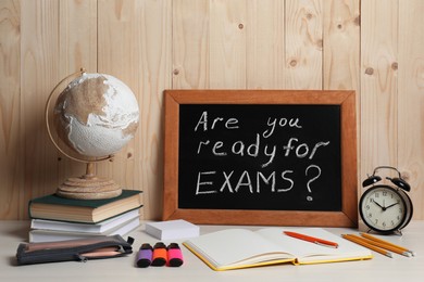 Photo of Blackboard with question Are You Ready For Exams? on white table near wooden wall