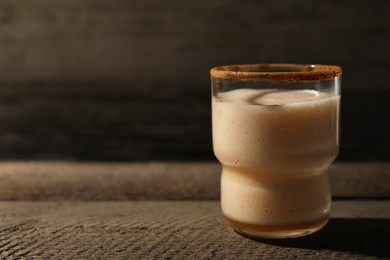 Photo of Glass of delicious eggnog on brown textured table. Space for text