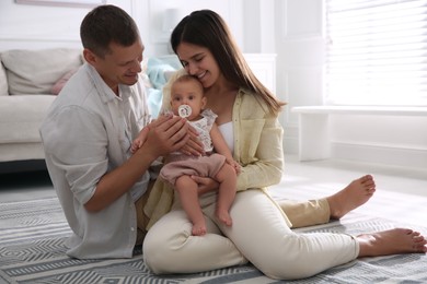 Photo of Happy couple holding their cute little baby with pacifier at home