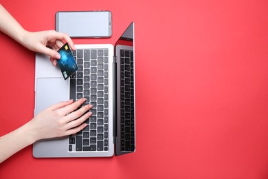 Online payment. Woman with laptop, smartphone and credit card on red background, top view. Space for text