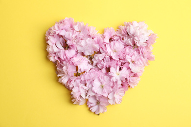 Photo of Heart made with sakura blossom on yellow background, top view. Japanese cherry