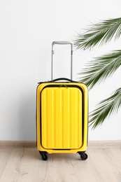 Photo of Bright yellow suitcase and palm branches near light wall indoors