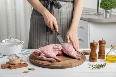 Photo of Woman cutting whole raw rabbit at white wooden table, closeup