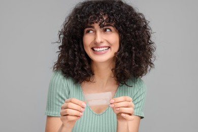 Photo of Young woman holding teeth whitening strips on grey background