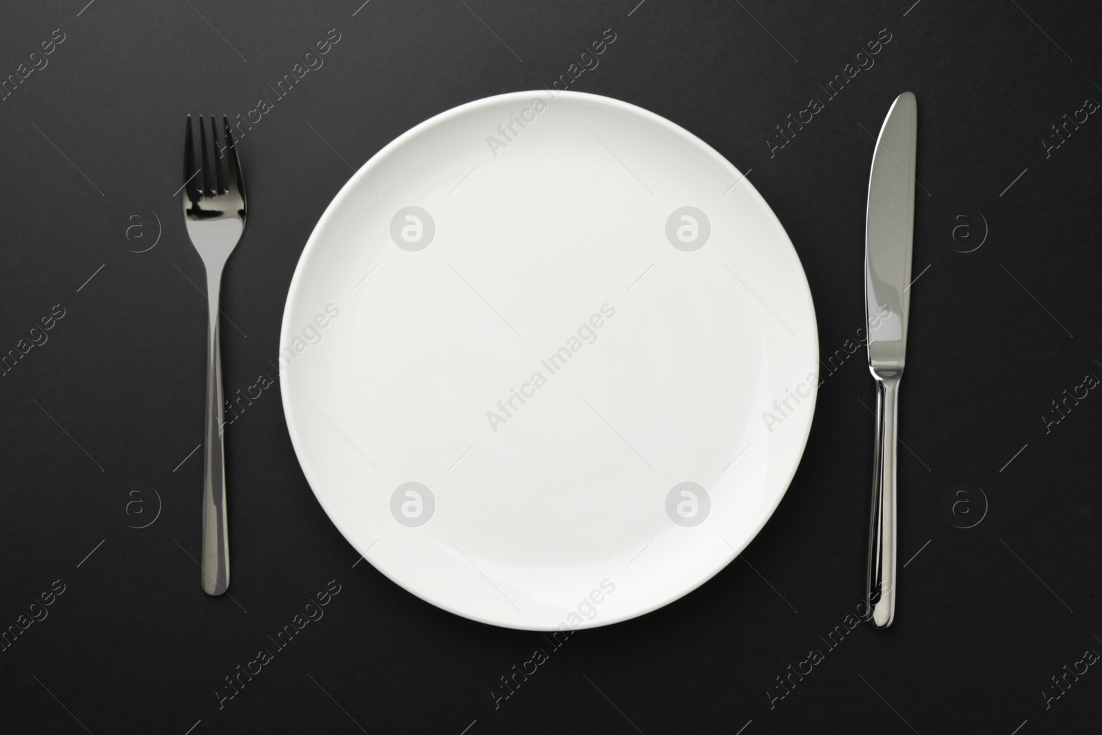 Empty plate, fork and knife on black table, top view Photo of Empty plate, fork and knife on black table, top view