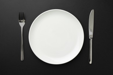 Photo of Empty plate, fork and knife on black table, top view